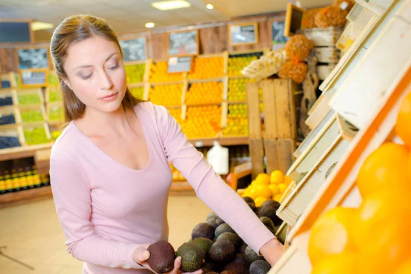 Damen i greengrocers väljer avokado päron — Stockfoto