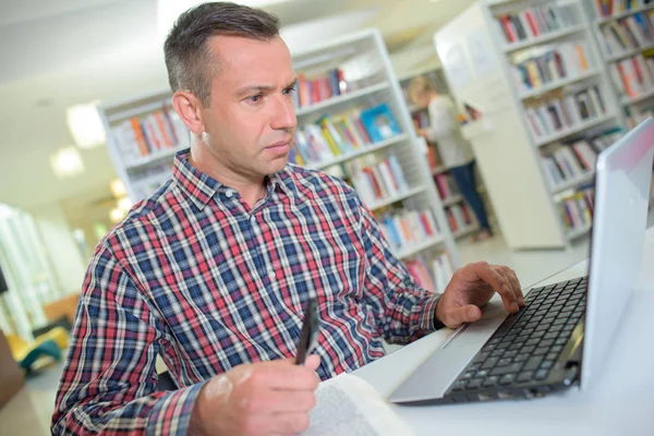 Ο άνθρωπος στη βιβλιοθήκη χρησιμοποιώντας φορητό υπολογιστή — Φωτογραφία Αρχείου