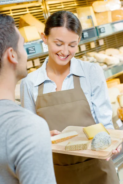 Shop assistant showing customer a tray of cheeses — Stock Photo, Image