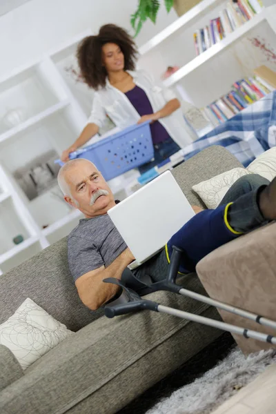 Female doing laundry at home while senior man is relaxing — Stock Photo, Image