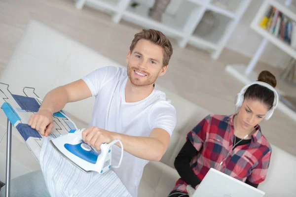 Happy boyfriend ironing while girlfriend relaxes — Stock Photo, Image