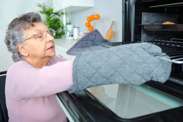 Пожилая женщина проверяет свою еду она приготовила в духовке — стоковое фото