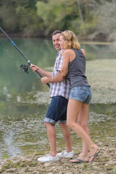 Pareja joven pescando de pie en la orilla del río — Foto de Stock