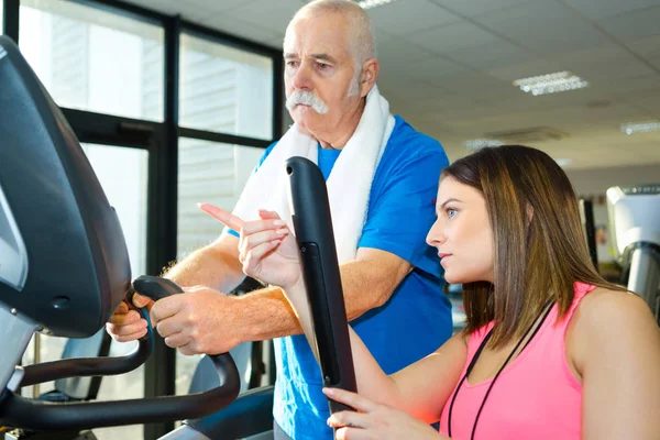 Senior man training in de sportschool met een personal trainer — Stockfoto