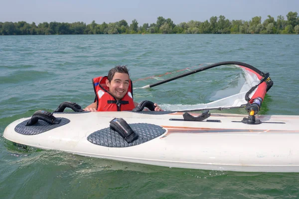 Hombre en el agua junto a la tabla de windsurf —  Fotos de Stock