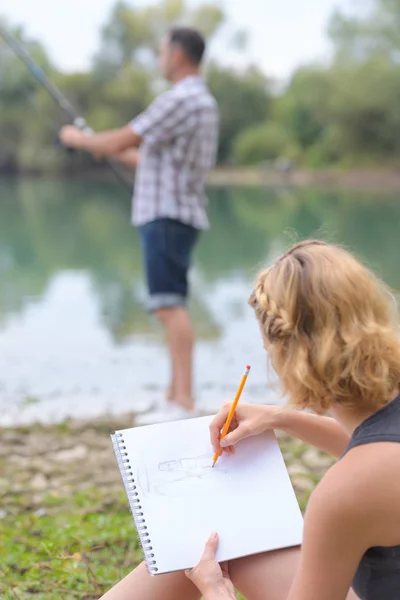 Frau zeichnet Freund beim Angeln auf Fluss — Stockfoto