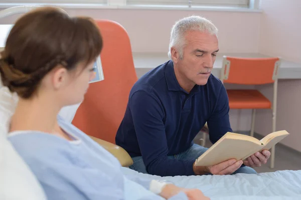 Чоловік читає книгу пацієнту в лікарняному ліжку — стокове фото