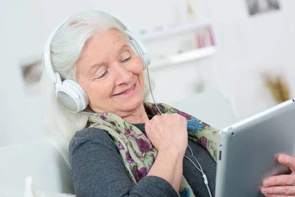 Улыбающаяся бабушка с наушниками слушает музыку — стоковое фото