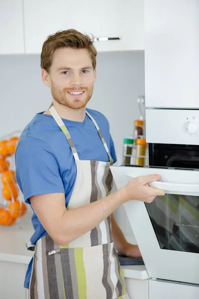 Jovem controla o forno na cozinha — Fotografia de Stock