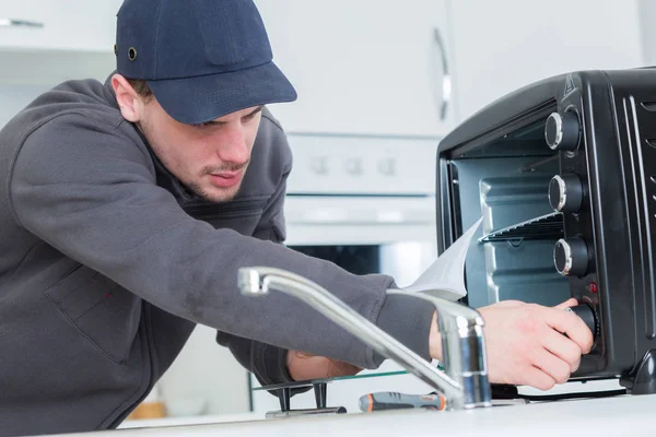 Jonge reparateur reparatie oven met schroevendraaier in klanten keuken — Stockfoto
