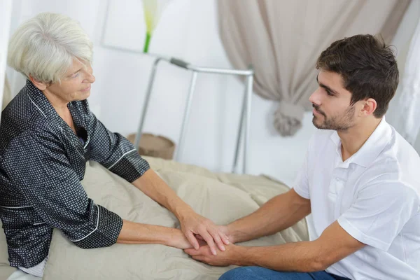 Seniorin und junge Betreuerin halten Händchen — Stockfoto