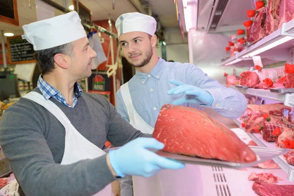 Carnicero sosteniendo una gran junta de carne en una bandeja — Foto de Stock