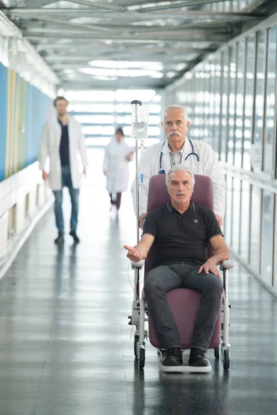Paciente en silla de ruedas empujada por un médico en el hospital —  Fotos de Stock