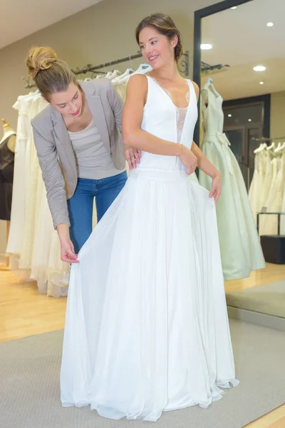 Fêmea tentando no vestido de noiva em uma loja com assistente — Fotografia de Stock