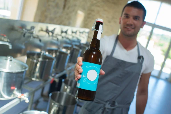 Cervejeiro bonito segurando uma garrafa de cerveja na cervejaria — Fotografia de Stock