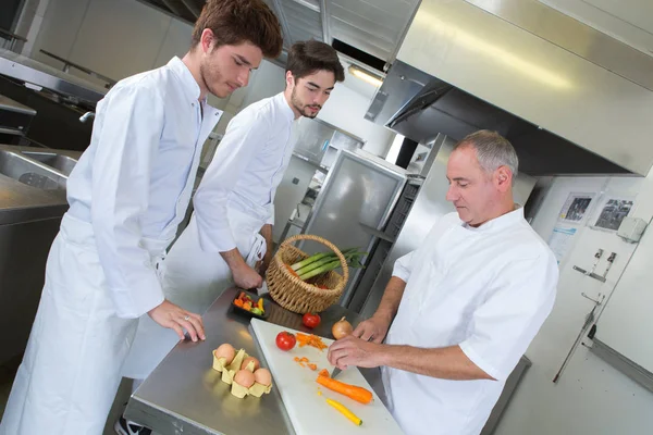 Cozinheiro e aprendizes em uma cozinha — Fotografia de Stock