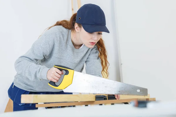 Mujer joven usando una sierra de mano en una carpintería — Foto de Stock