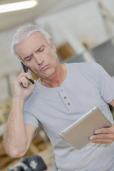 Hombre mirando tableta, por teléfono, expresión confusa — Foto de Stock