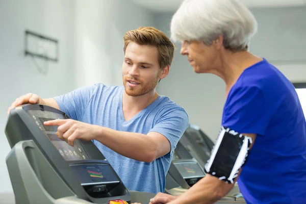 Senior kvinna gör övning på en cykel med unga tränare — Stockfoto