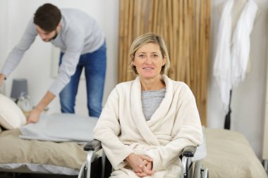 happy women in wheelchair with male assistant at home clipart