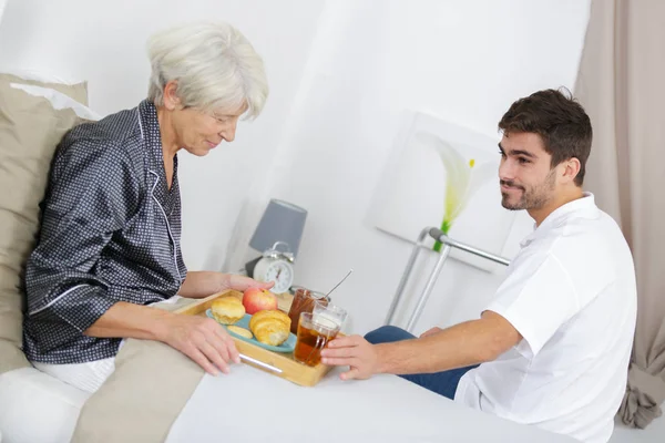 Jonge Man Serveert Ontbijt Bed Voor Oudere Dame — Stockfoto