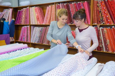 beautiful female workers choosing fabric skeins in textile shop clipart