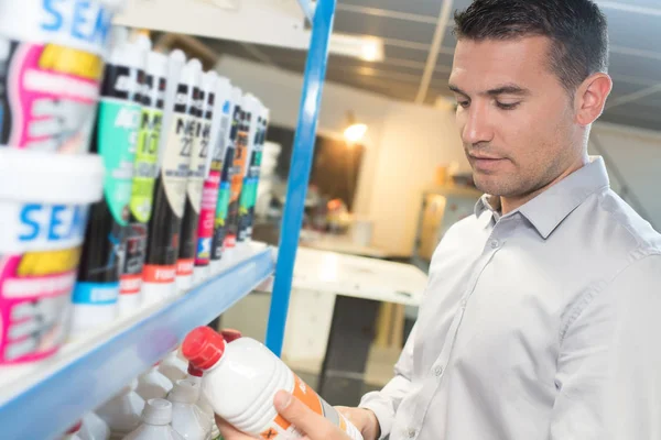 young man choosing household chemicals in supermarket