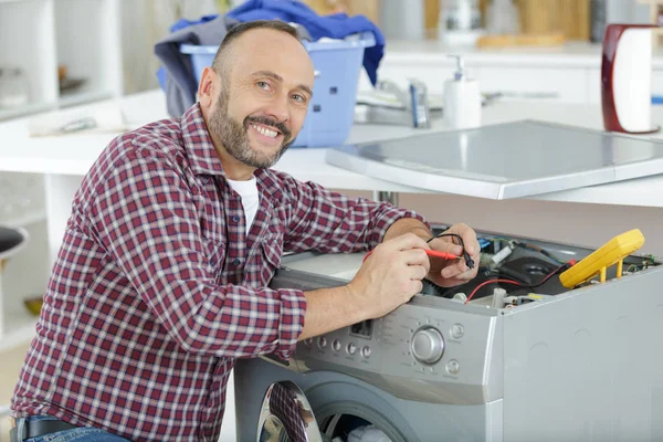 Werkende loodgieter repareert een wasmachine in de wasserij — Stockfoto