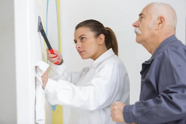 Female apprentice scraping wall under supervision — Stock Photo, Image
