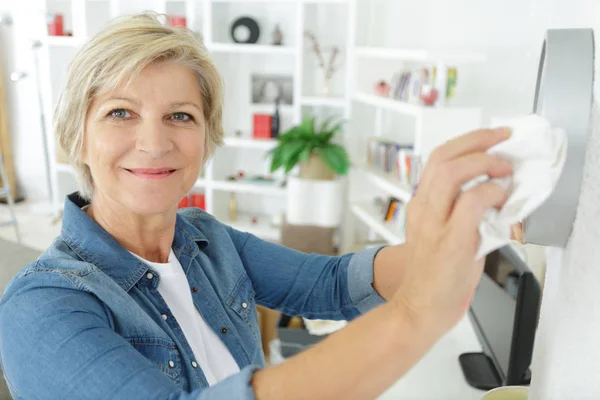 Reife Frau staubt ihr Haus — Stockfoto