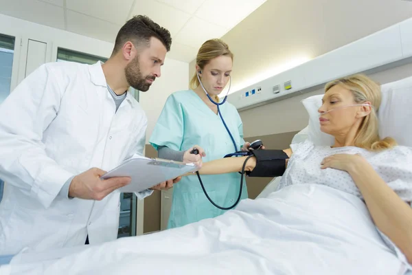 病院のベッドで成熟した女性の血圧を取る思いやりのある医者 — ストック写真