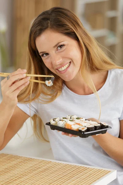 Vacker ung kvinna med sushi rulle hemma — Stockfoto