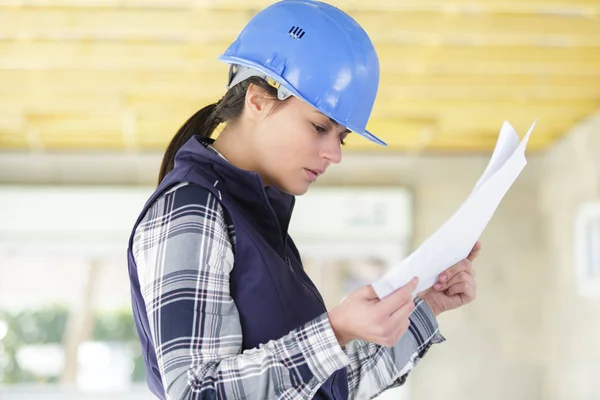 Construtor feminino olhando para papelada no local — Fotografia de Stock