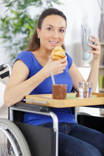 Sorridente donna storpia seduta su una sedia a rotelle a fare colazione — Foto Stock