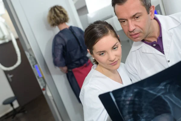 Pessoal médico olhando para o raio-x como paciente fica por aparelho — Fotografia de Stock
