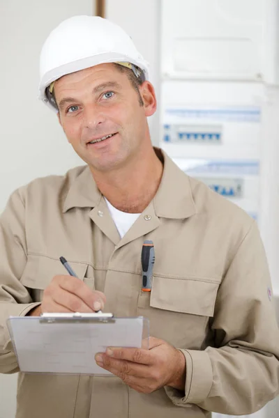 Hombre concentrado constructor en la escritura del casco del edificio en portapapeles —  Fotos de Stock