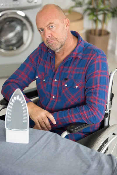 Disabled man on wheelchair ironing clothing — Stock Photo, Image