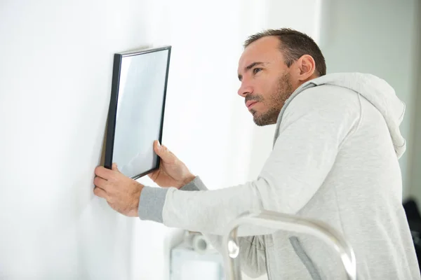 Retrato del hombre colgando imagen en blanco en la pared — Foto de Stock