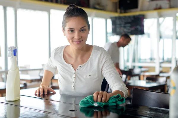 Porträt einer lächelnden Kellnerin, die Theke in Bar putzt — Stockfoto