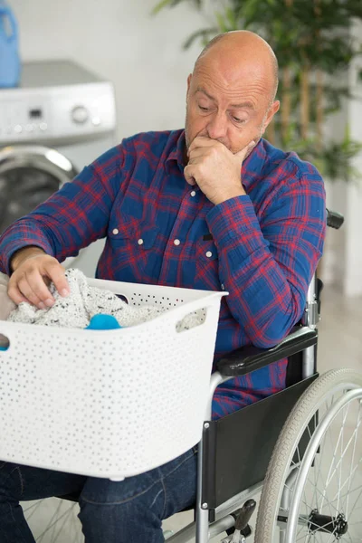 Funktionshindrade man tittar igenom korg med tvätt med förvirring — Stockfoto