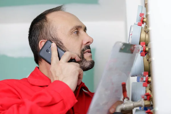 Serviceman ficou por medidores de água falando no smartphone — Fotografia de Stock