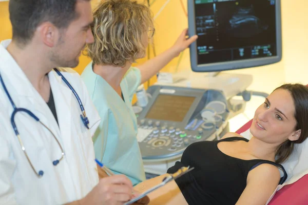 Doctor tomando notas de la mujer que tiene ultrasonido —  Fotos de Stock