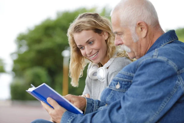 Young woman reading book in the park disabled senior man — Stock Photo, Image