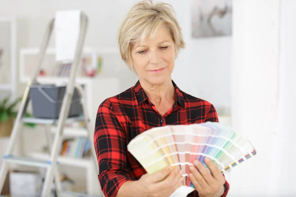 Happy senior woman choosing color from swatches — Stock Photo, Image