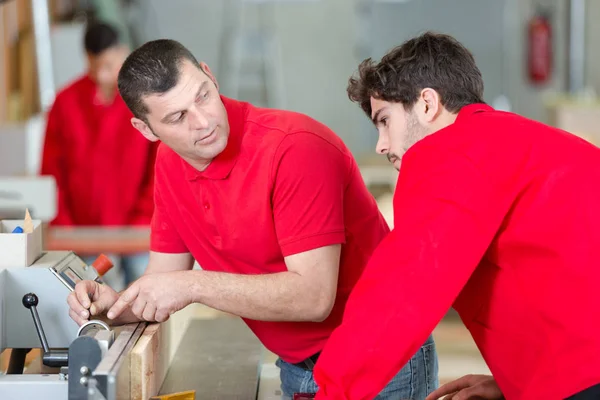 Mann zeigt Auszubildenden, wie man Maschine in Werkstatt einrichtet — Stockfoto