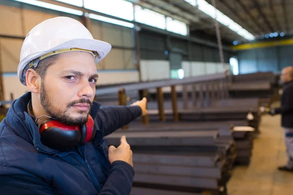 Manlig fabriksarbetare som pekar till travar av belägger med metall — Stockfoto