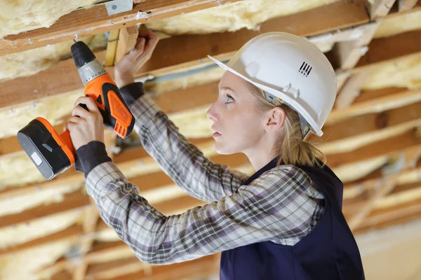 Ženská stavitel používající akumulátorový vrták na dřevěné stropní trámy — Stock fotografie