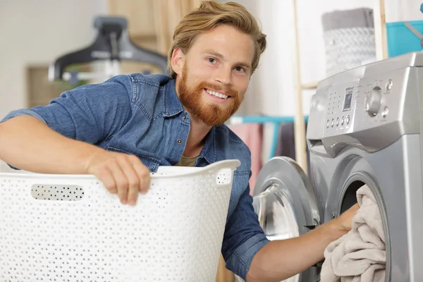 Ung man lastar kläder i tvättmaskin i köket — Stockfoto