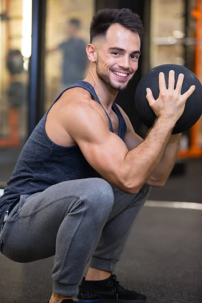 Hombre sosteniendo una pelota haciendo sentadillas en el gimnasio — Foto de Stock