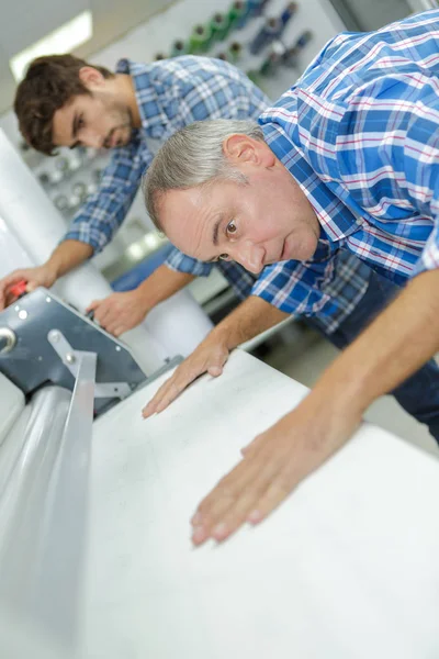 Werknemer die materiaal uitlijnt onder machine — Stockfoto